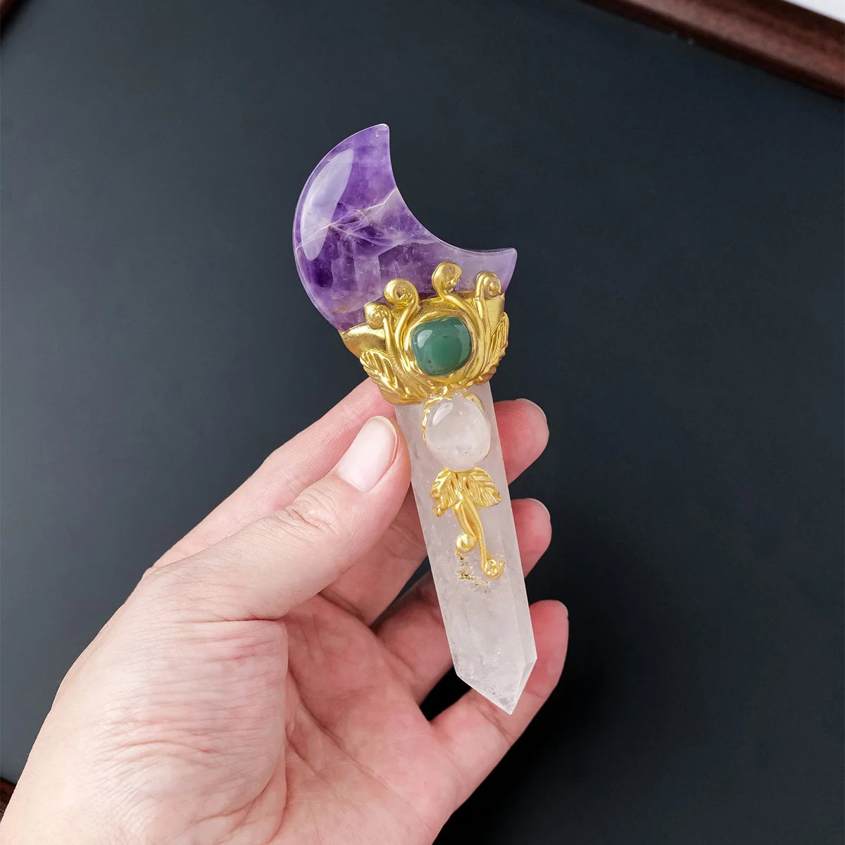 A hand holds a natural crystal moon and star scepter wand featuring purple amethyst, green jade, and clear quartz elements.