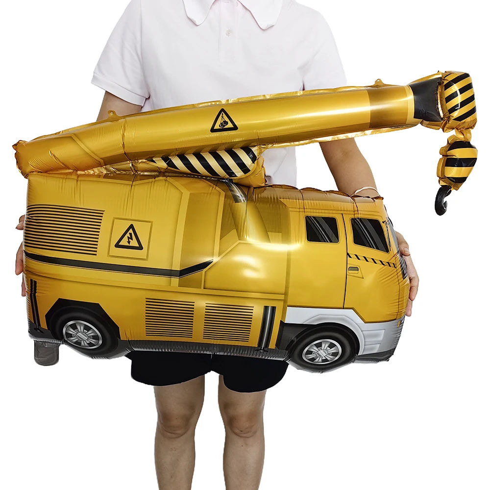 A golden construction truck foil balloon is being held by a person for party decoration.