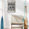 A distressed metal wall sign with text about happiness and buying a lake home, displayed on a white wall.