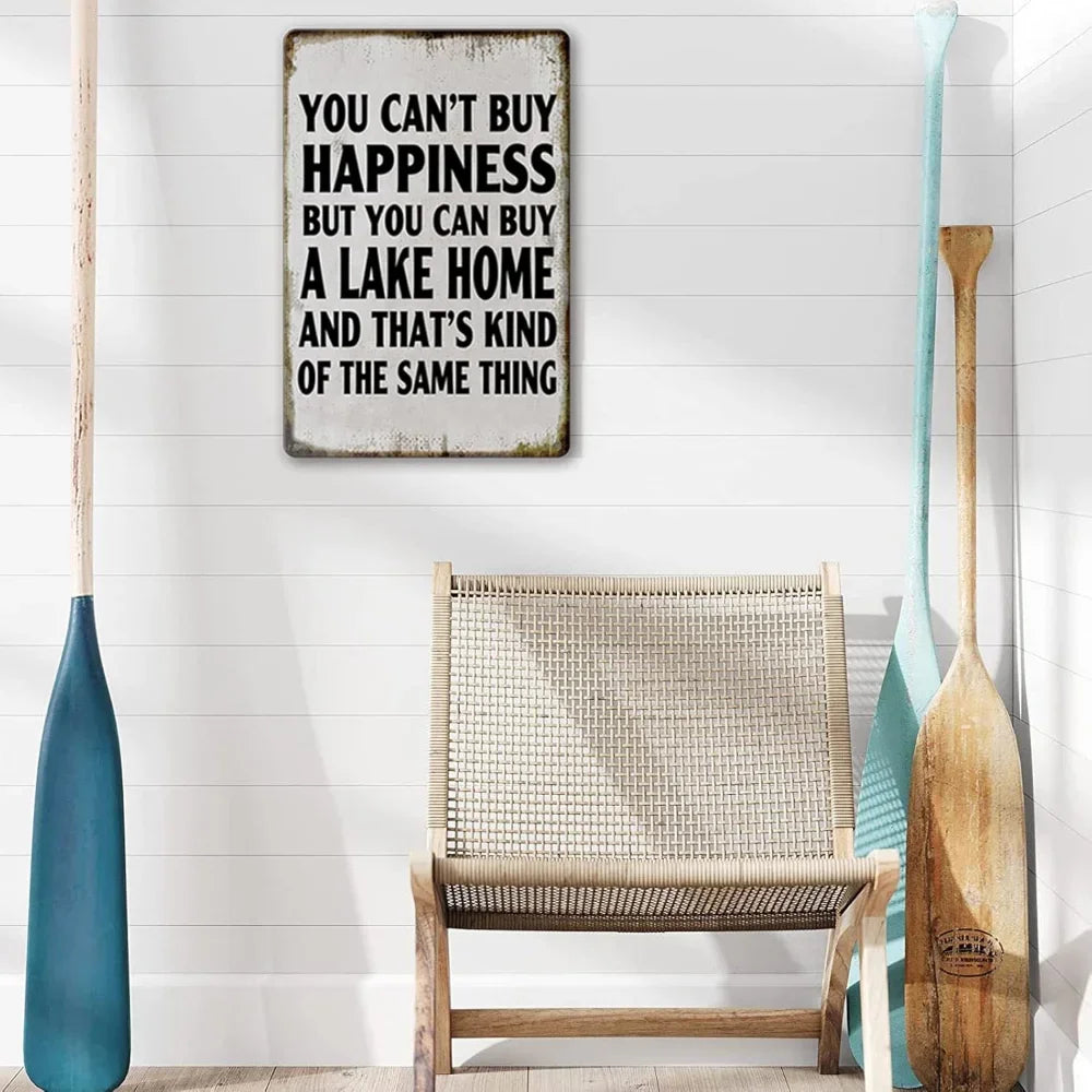 A distressed metal wall sign with text about happiness and buying a lake home, displayed on a white wall.