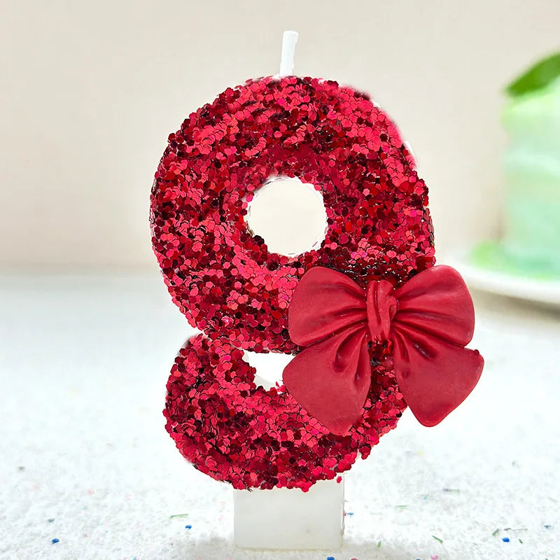 A large number eight made of red glittery sequins and a matching red bow, displayed on a white candle.