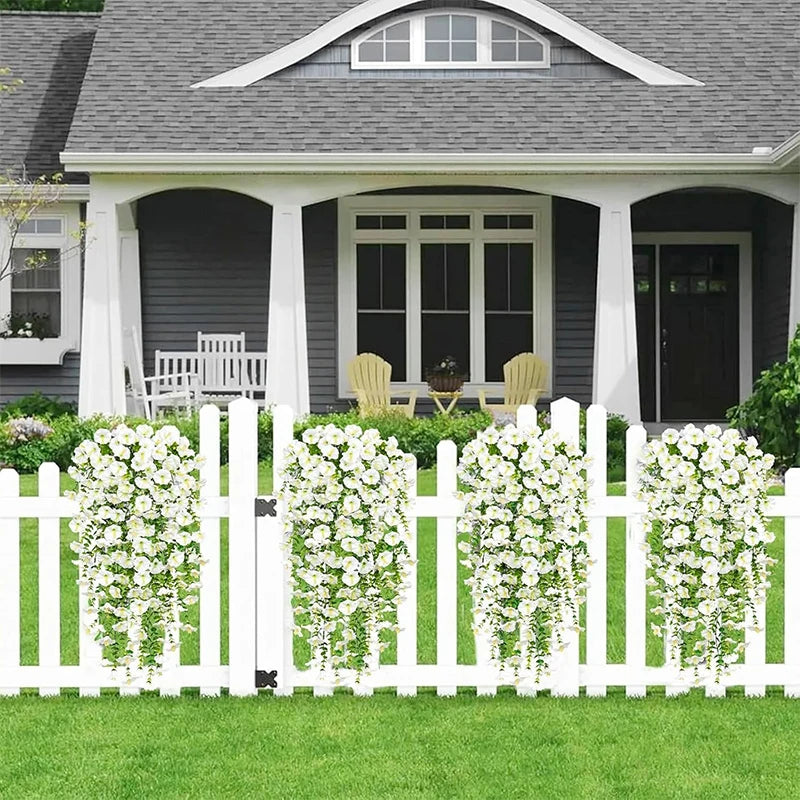 White picket fence with hanging white morning glory vines in a green lawn and house backdrop