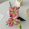 Three pink and white artificial lilies with buds arranged on a white surface.