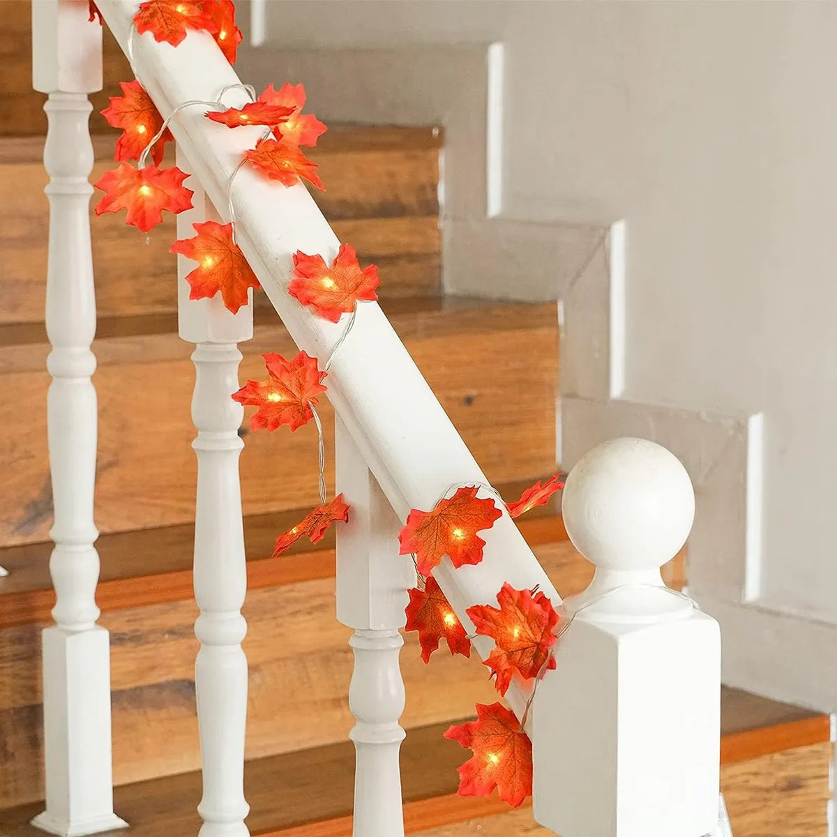 White railing decorated with warm orange maple leaf fairy lights on a wooden staircase.