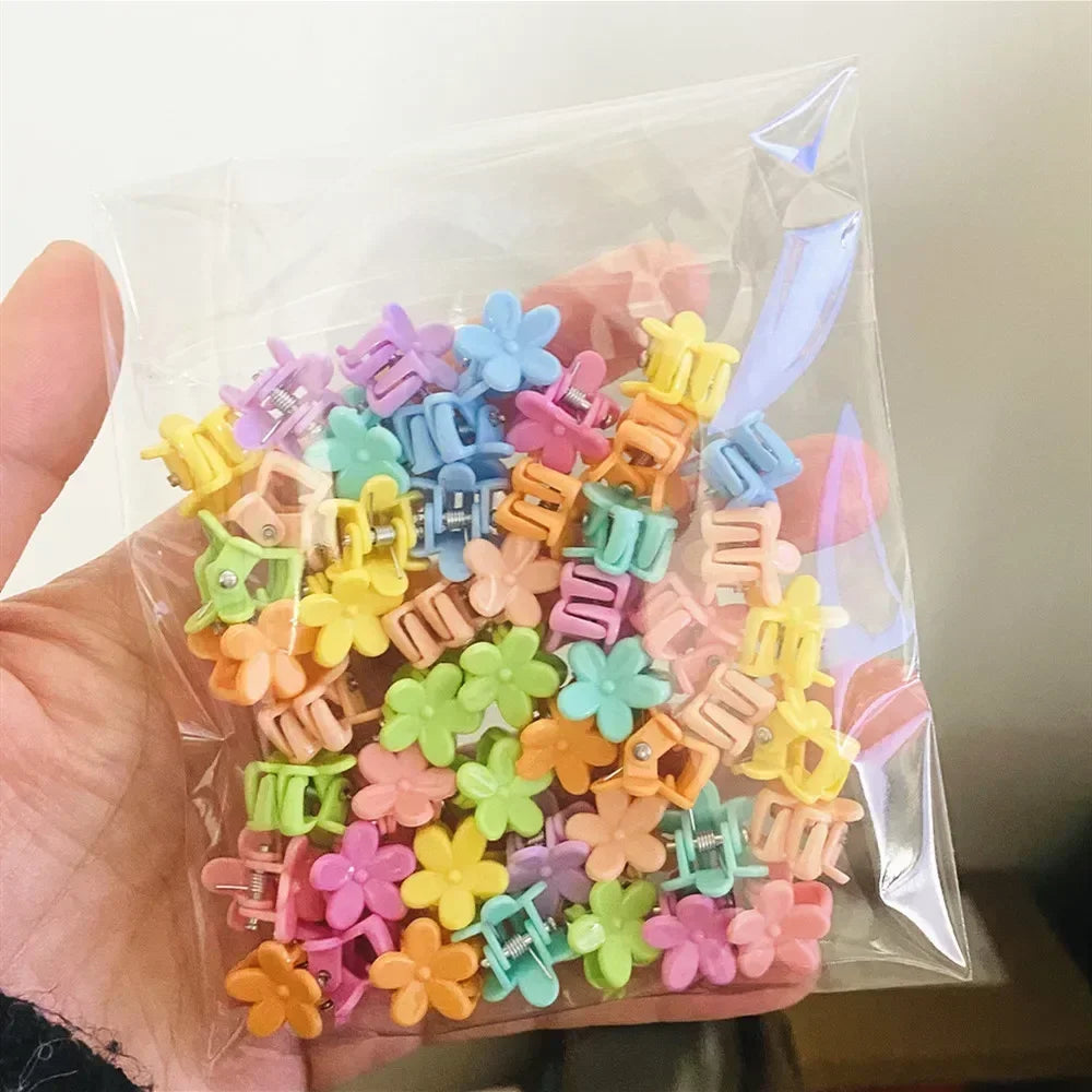 A hand holds a clear plastic bag filled with colorful flower and star hair claw clips for kids.