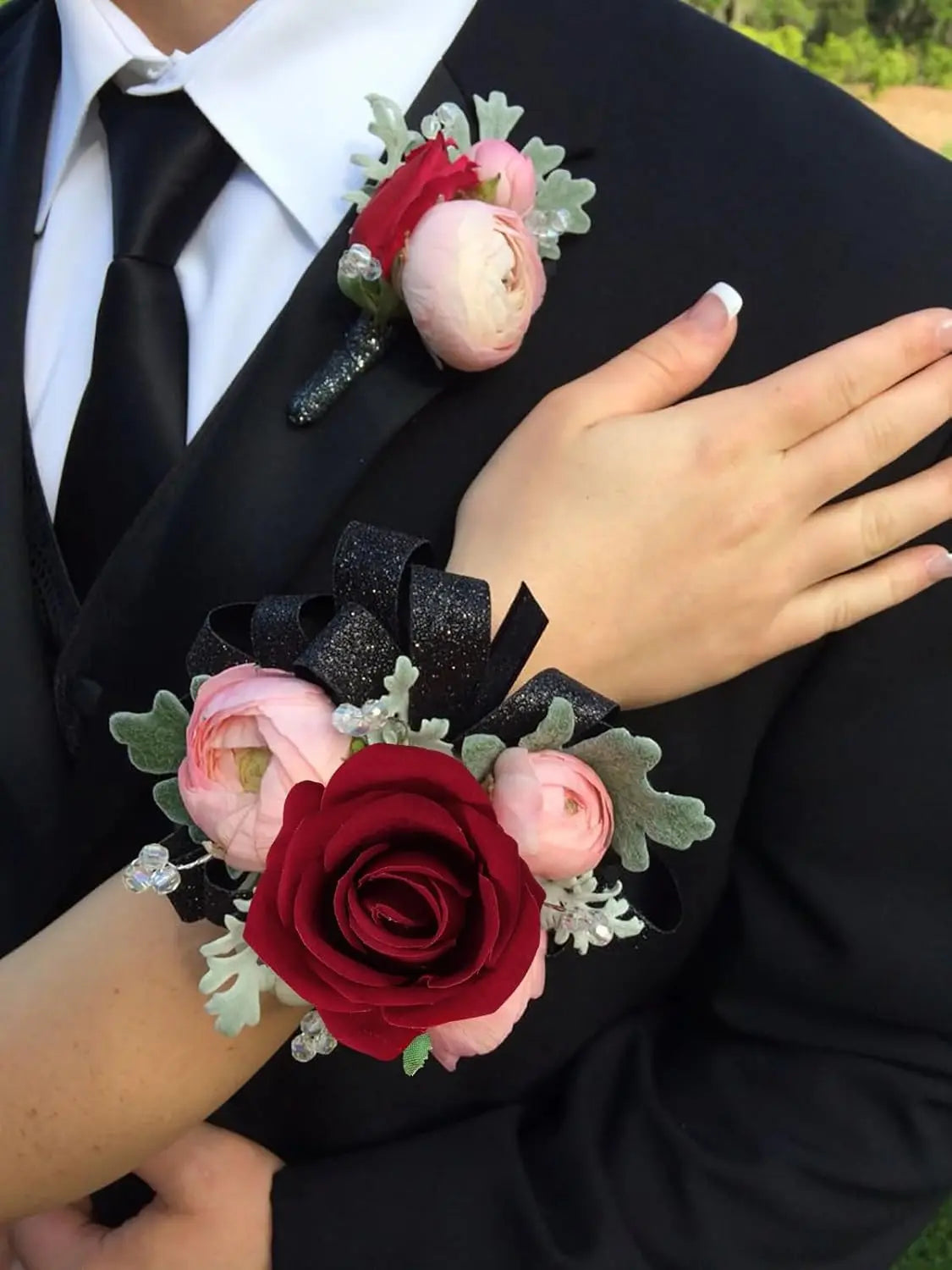 A hand holds a bouquet of artificial roses featuring pink and deep red blooms with dark foliage.
