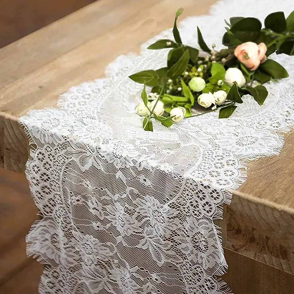 Un camino de mesa de encaje floral vintage con hojas verdes y flores blancas sobre una mesa de madera.