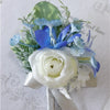A small boutonniere featuring a white rose accented with dusty blue and light blue silk flowers and greenery.