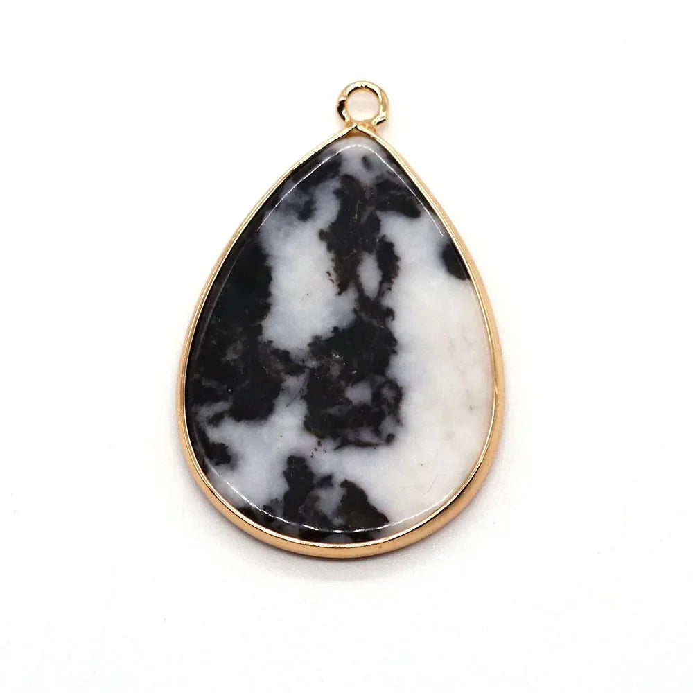 A teardrop-shaped pendant charm made of black and white marble set in a gold-colored bezel.