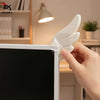 A hand is attaching a white, wing-shaped decoration to the side of a black monitor screen.