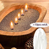 A wooden bowl filled with dark, pearled material and several lit candles on a wooden surface.