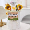 A white cake decorated with a handmade crochet flower bouquet featuring yellow and orange flowers and a small white dog figur