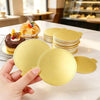 Une main tient un plateau réutilisable pour dessert de couleur or, entouré d'empilements similaires et d'un gâteau décoré.