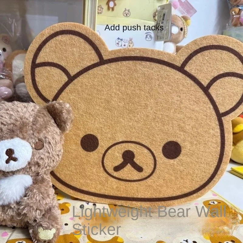 A felt wall decor panel shaped like a bear face with large ears and a nose, displayed next to a plush teddy bear.