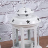 A white vintage hanging metal lantern with a glass enclosure and a decorative lid featuring black stars.