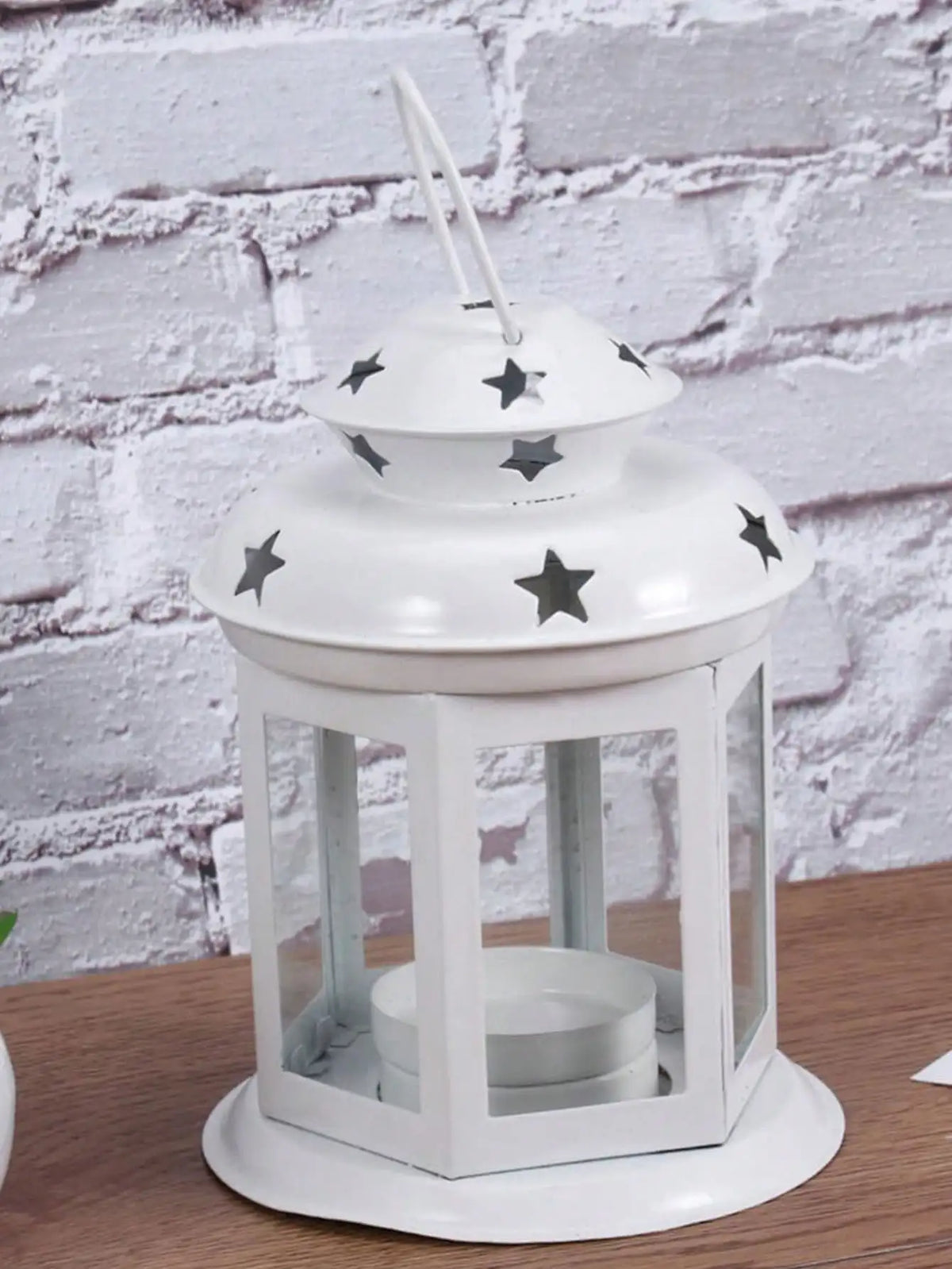 A white vintage hanging metal lantern with a glass enclosure and a decorative lid featuring black stars.
