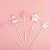 A set of pink and white star-shaped cake toppers for birthday parties arranged on a pink background.