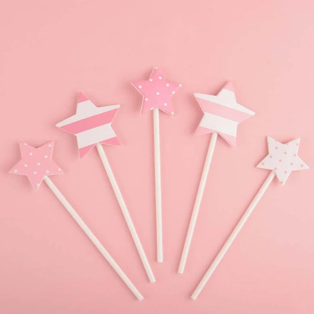 A set of pink and white star-shaped cake toppers for birthday parties arranged on a pink background.