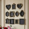 A collection of vintage baroque resin hanging photo frames in black and gold on a cream-colored wall.
