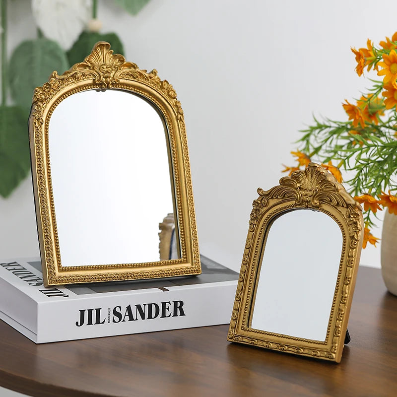 A vintage gold-framed arched vanity mirror resting on a white box with the name Jil Sander.
