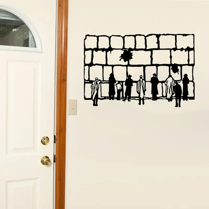 Schwarzer dekorativer Metallzaun mit Silhouetten von Menschen und Vegetation an einer weißen Wand.