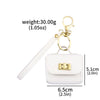 A white mini leather openable bag with a gold-tone keychain attached to a white strap.