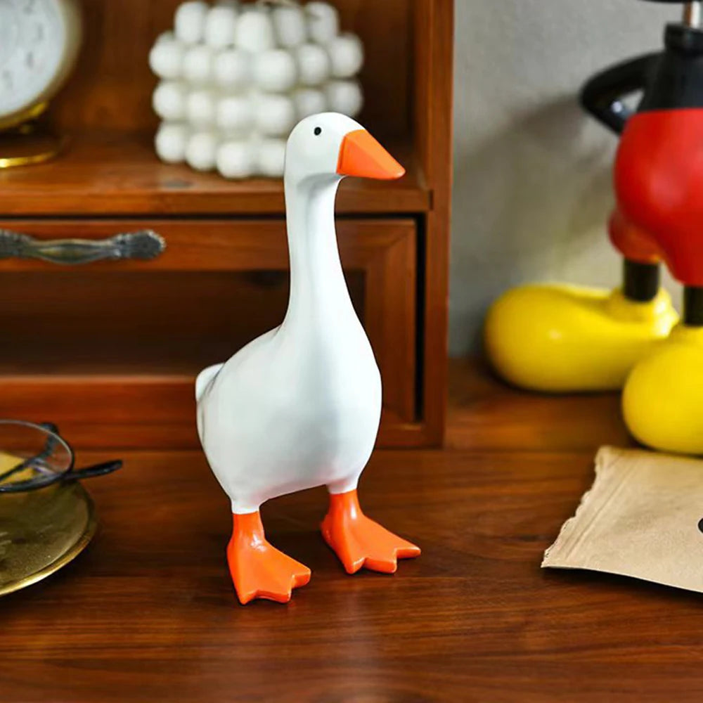 A white ceramic goose key holder with orange feet sitting on a wooden surface.