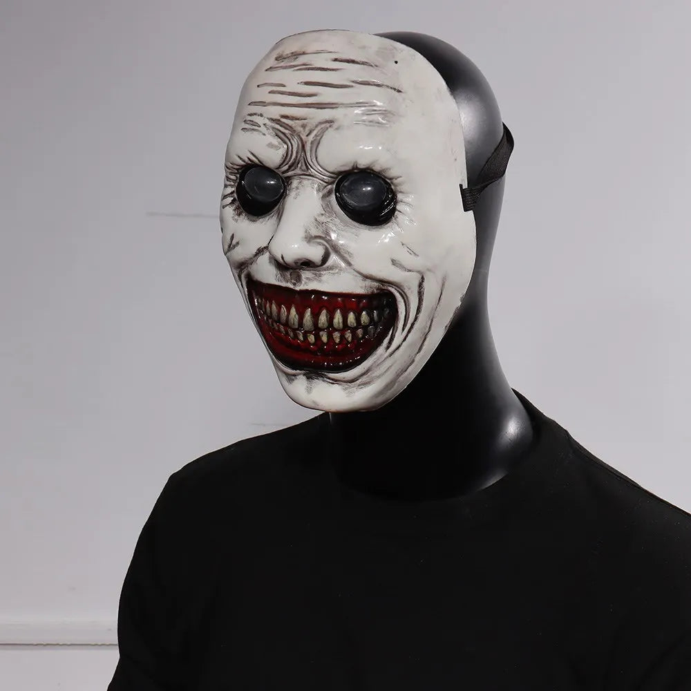 A white demon mask with a wide, menacing grin and dark eyes displayed on a black mannequin.