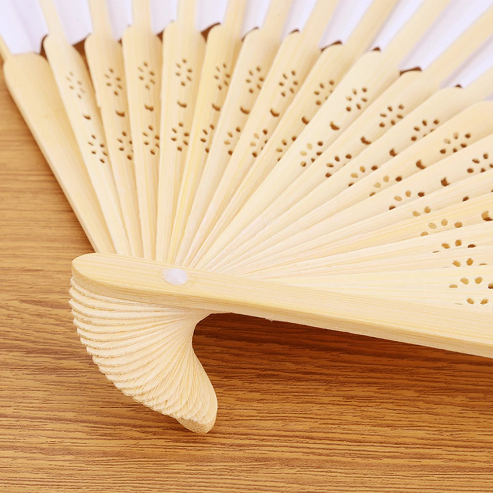 A light wood bamboo folding fan with delicate perforations, shown in a close-up on a wooden surface.