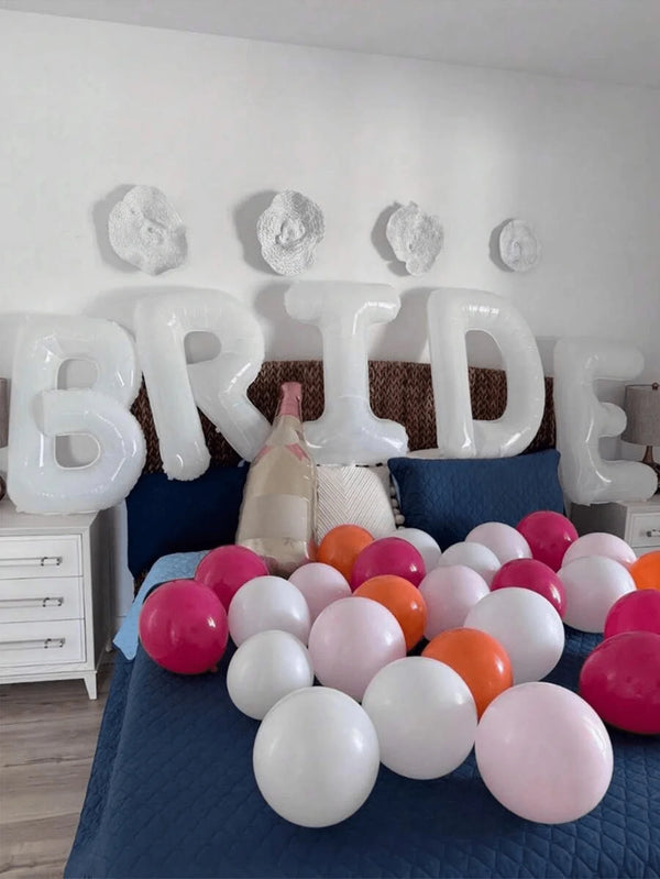 Un ensemble de ballons en feuille blanche formant le mot BRIDE, posés sur un lit avec des draps bleus.