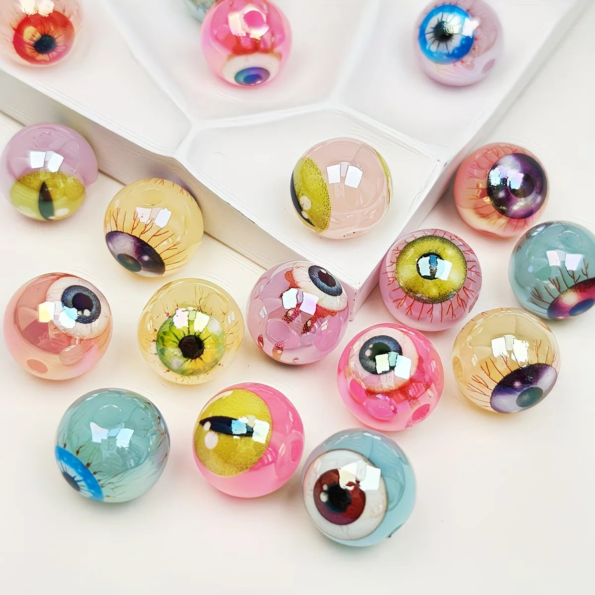 A collection of glossy, double-sided eyeball beads in various colors and shades arranged in a white tray.