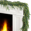 Green Norfolk pine Christmas garland with warm lights draped over a white fireplace mantel