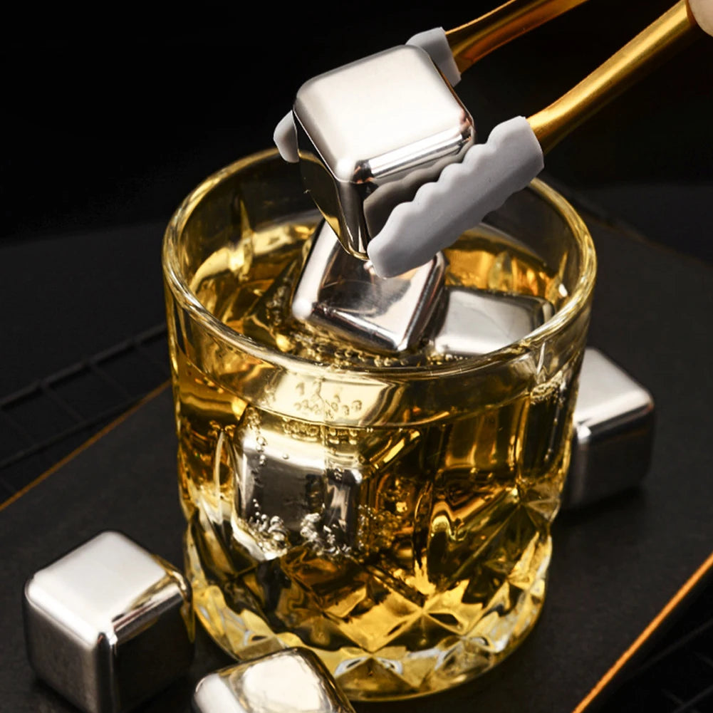 Reusable stainless steel ice cubes being dropped into a glass of amber whiskey
