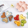 A heart-shaped four-compartment snack tray filled with various nuts, candies, and dried fruits.