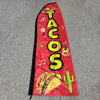 A red feather flag advertising banner with yellow text spelling TACOS and colorful illustrations of food items.