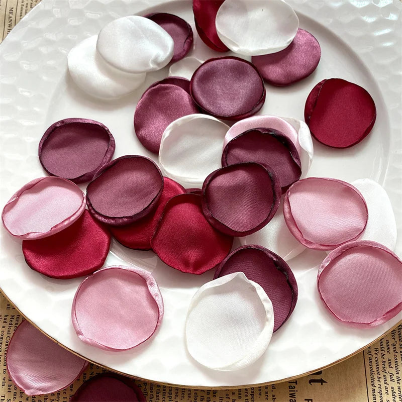 A collection of silk rose petals in shades of pink, magenta, and white arranged on a white plate.