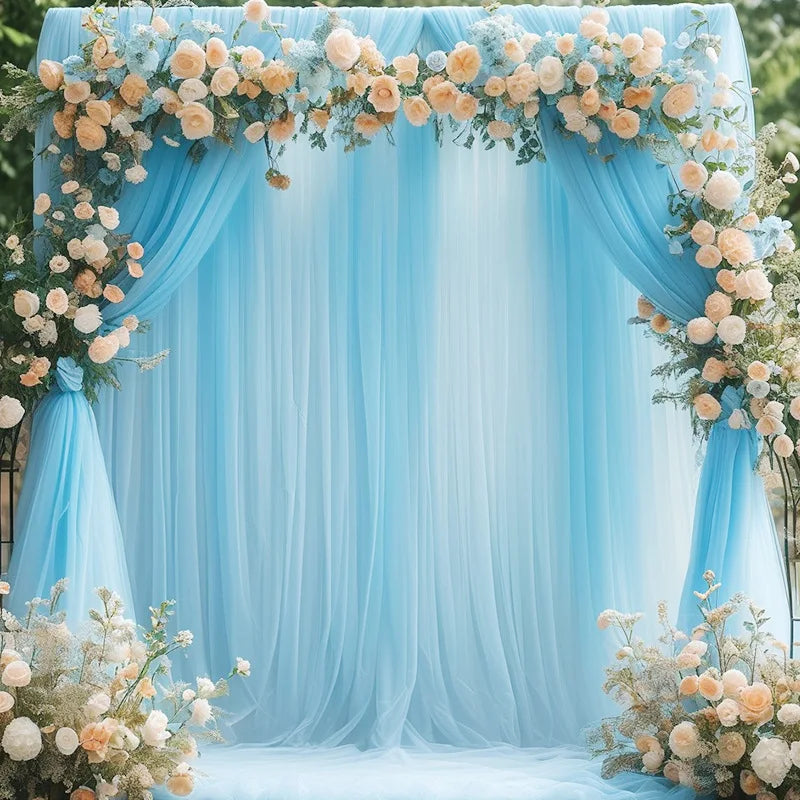A light blue tulle backdrop decorated with floral garlands and draped fabric for an elegant event.