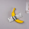 A yellow banana shape is crossed by a silver ribbon, displayed on a light gray background.