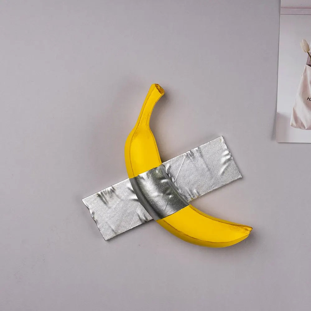 A yellow banana shape is crossed by a silver ribbon, displayed on a light gray background.