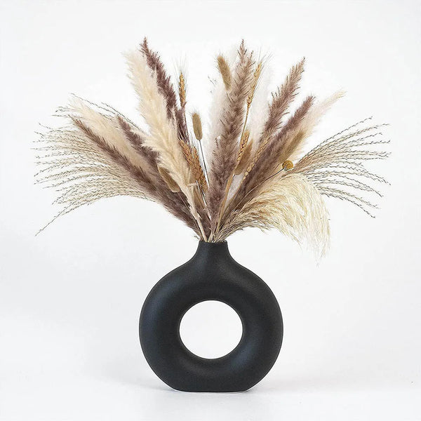 A black ceramic donut-shaped vase holding dried pampas grass and wheat stalks.