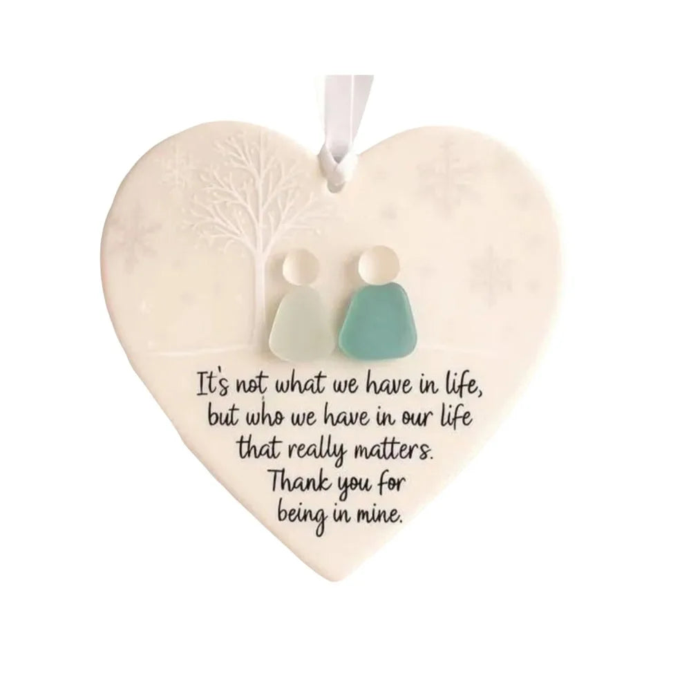 A heart-shaped acrylic pendant featuring three frosted figures with a tree design and text that reads It's not what we have i
