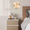 A round gold vinyl record wall clock hangs above a bedside table with a white lamp and bedding.