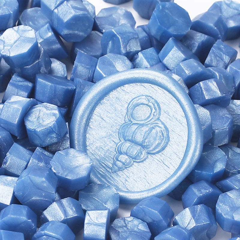Blue transparent wax sealing beads scattered on a white background with one bead featuring an elephant design