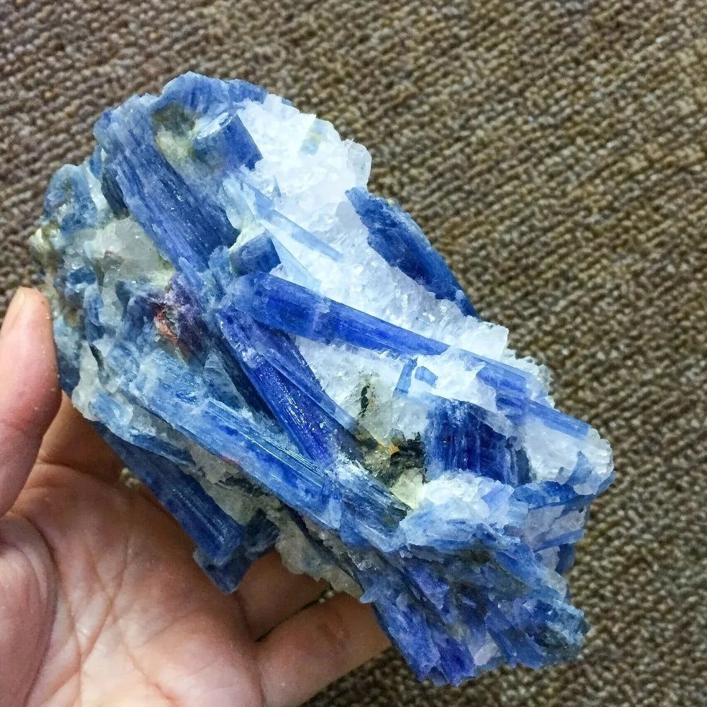 A hand holds a deep blue kyanite crystal specimen with sharp facets on a brown fabric background.