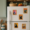 Refrigerador blanco decorado con varios cuadros enmarcados de gatos y paisajes.