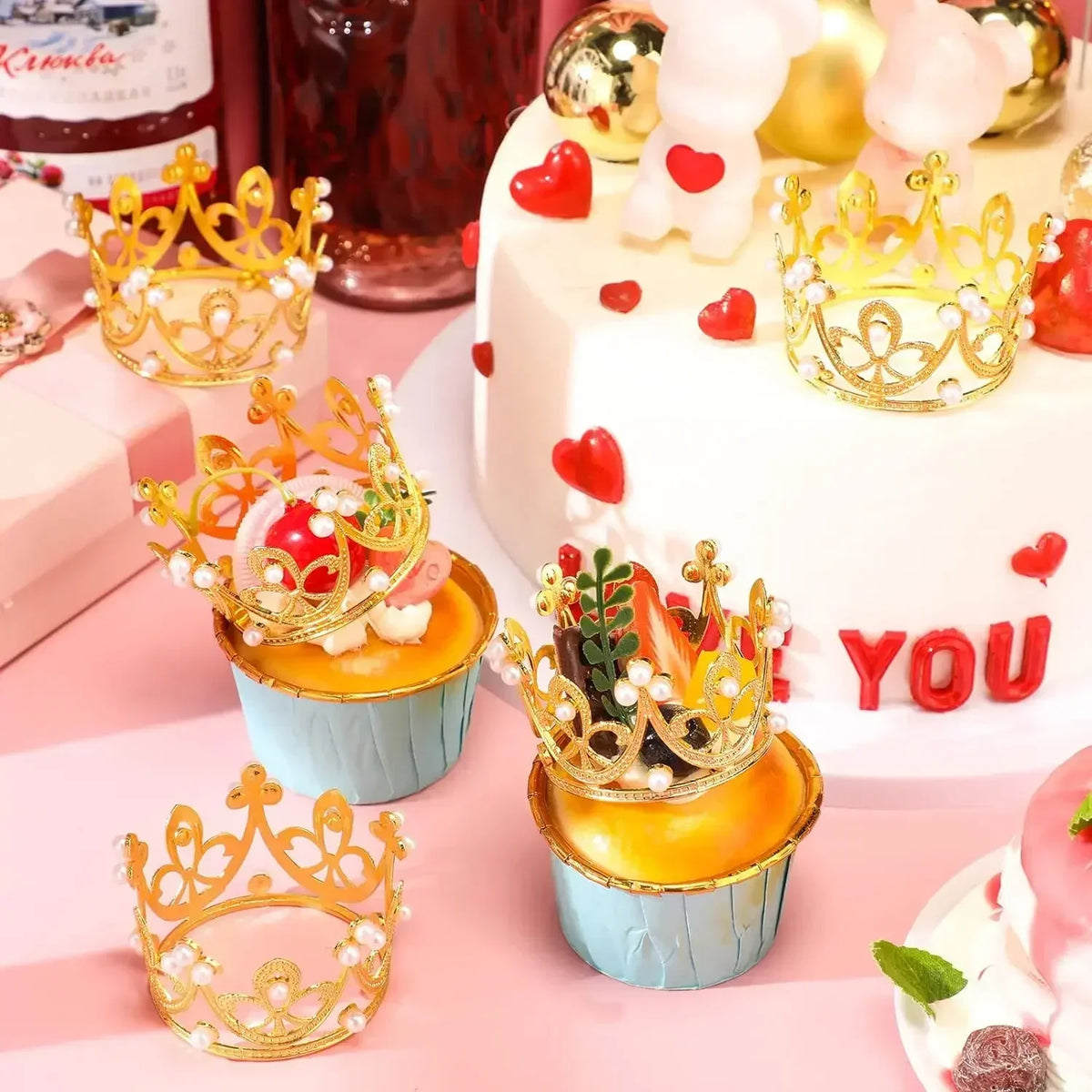 A display of mini gold and silver crown cake toppers and decorations on a pink platter.
