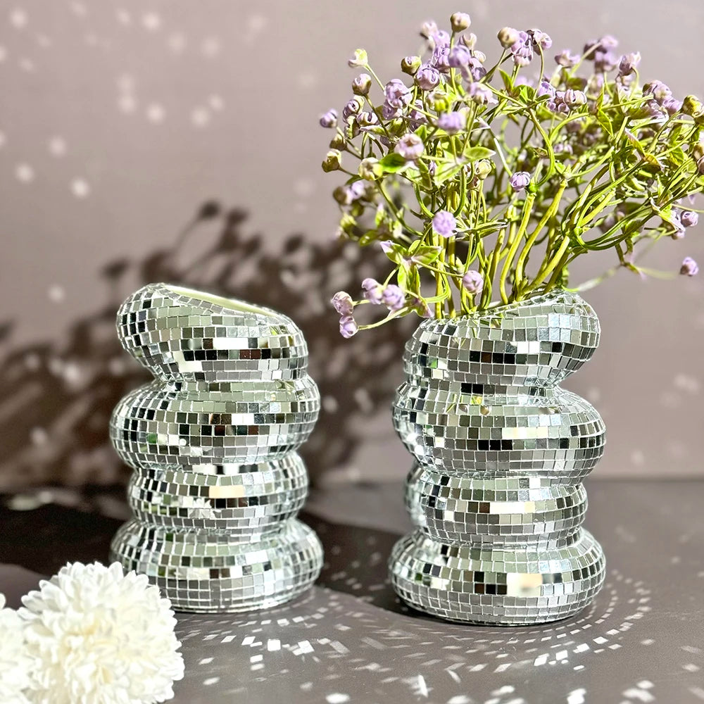 A clear mirror tile disco ball vase filled with purple flowers, set against a gray background.