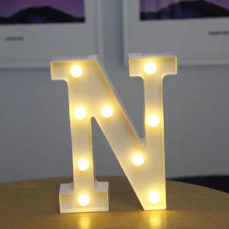 A glowing warm white LED alphabet letter light shaped like the letter N resting on a wooden surface.