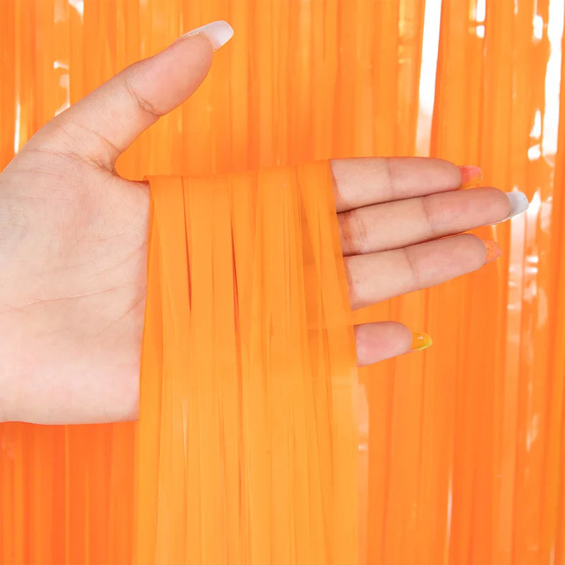 Hand holding metallic orange tinsel foil fringe curtain backdrop for parties