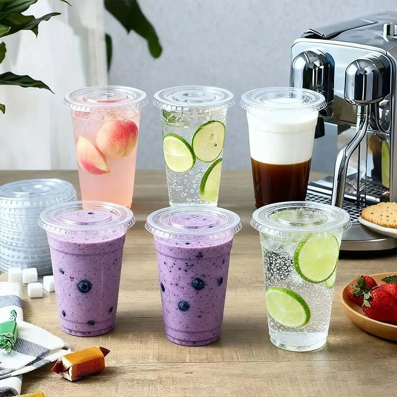 A collection of purple and green fruit smoothies in clear plastic cups, next to a silver coffee machine.